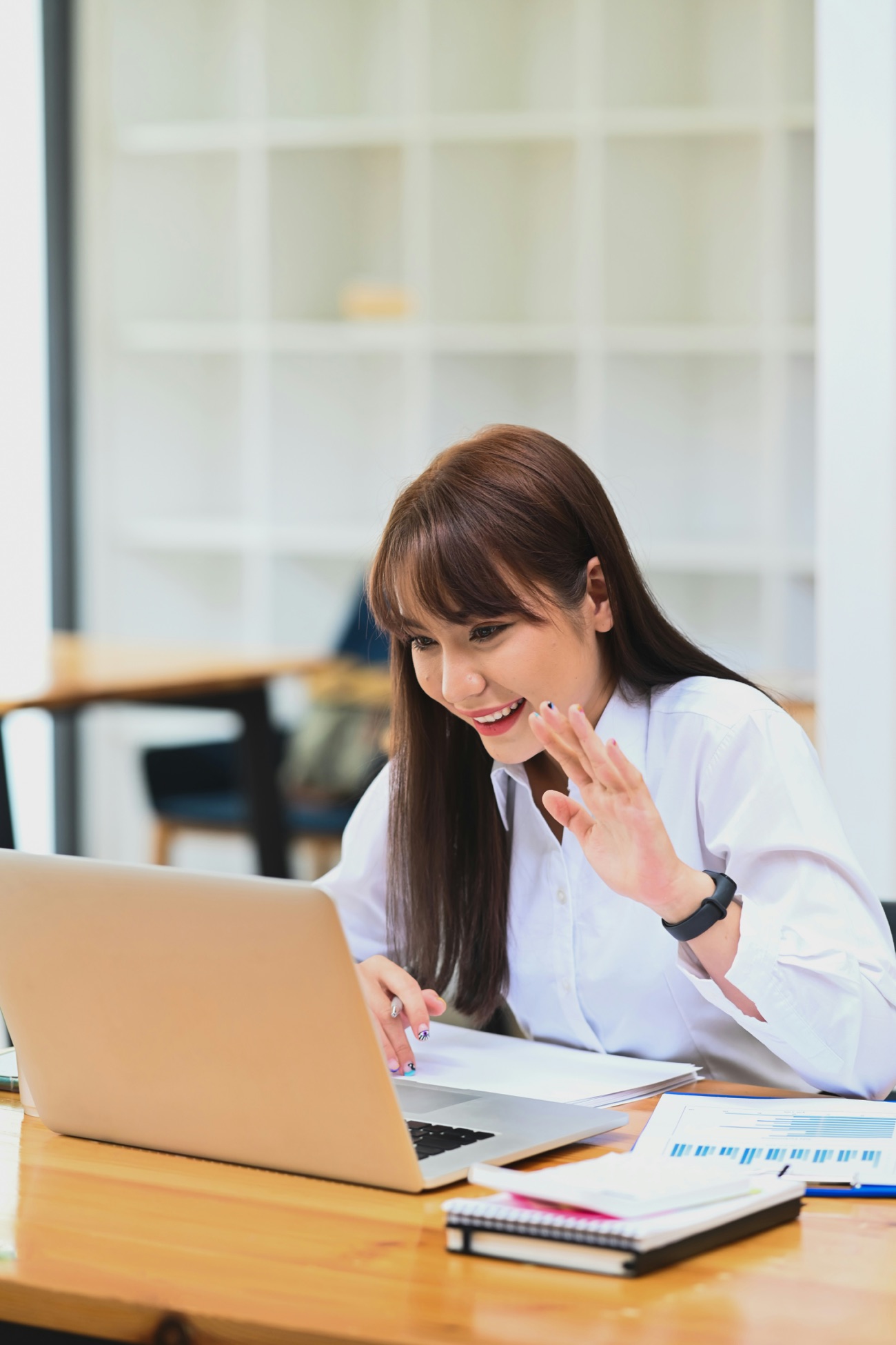 A team member smiling and waving during a warm welcome video call at her desk.