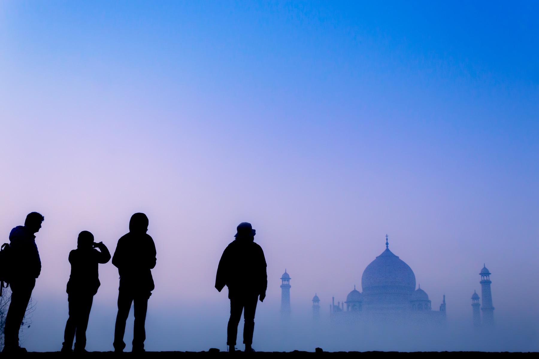 Silhouettes of people watching the Taj Mahal at dawn.