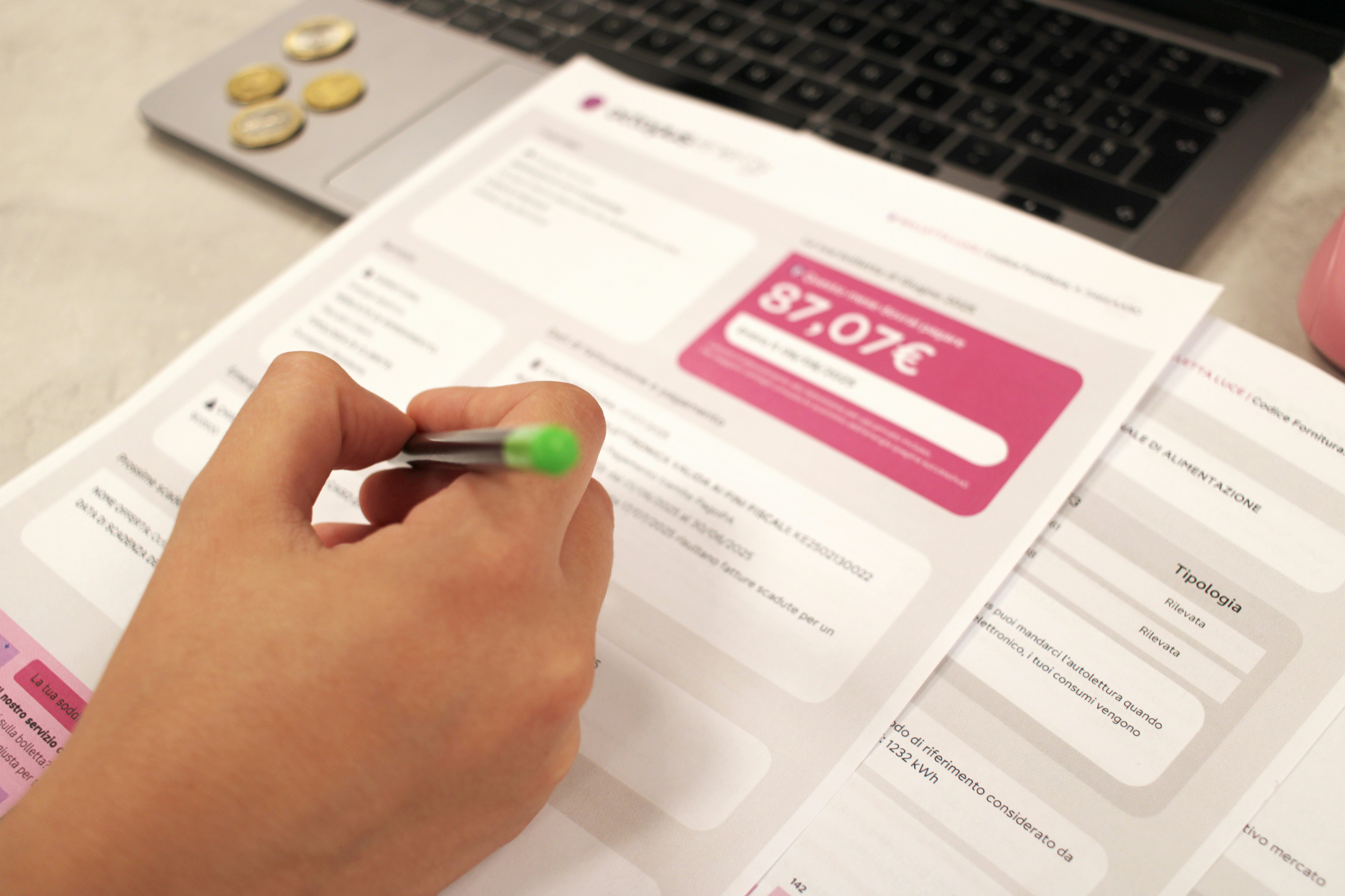 A hand reviewing an itemised bill with a highlighter, beside a laptop and coins.