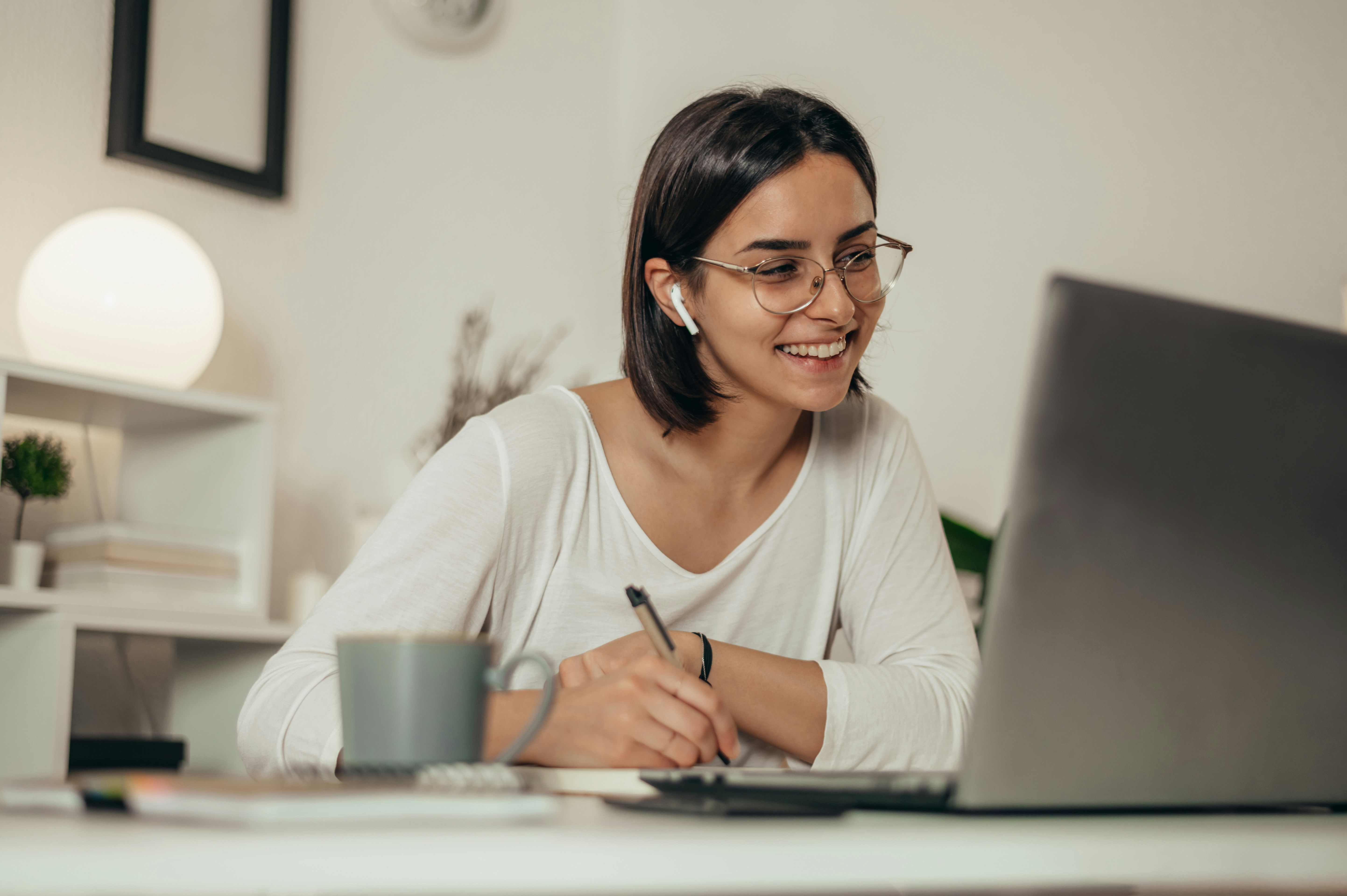 A new hire smiling at her laptop while taking notes on her first day.