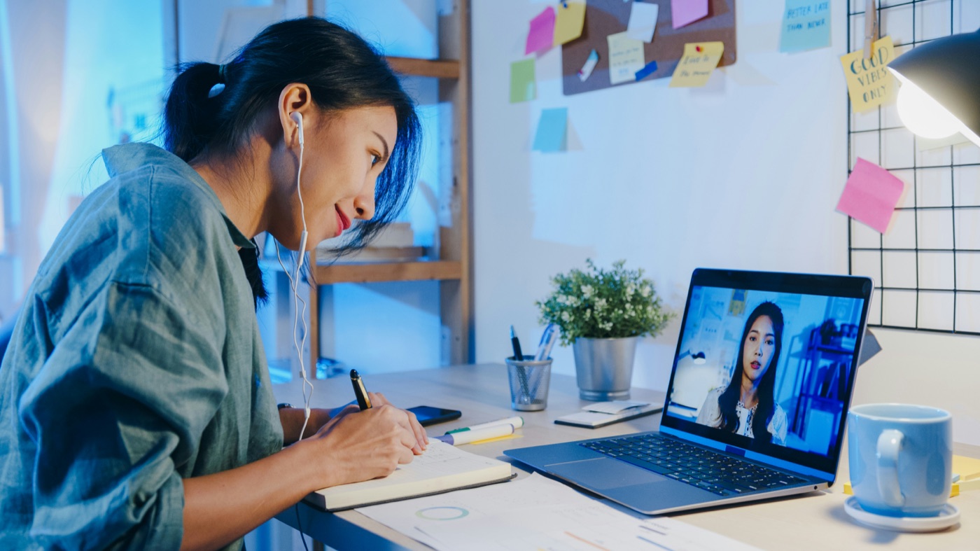 A recruiter taking notes during a live video interview with a candidate on her laptop.